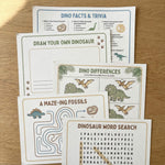 OneStopBox dinosaur themed kids party activity sheets including word search, spot the difference and colouring sheet, laid out on a timber surface.