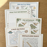 OneStopBox dinosaur themed kids party activity sheets including word search, spot the difference and colouring sheet, laid out on a timber surface.