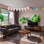 Living room decorated for a kids dinosaur birthday party with green printed balloons, triangle bunting, dinosaur character banner, happy birthday sign, light box and table cover from a OneStopBox party decorations kit.