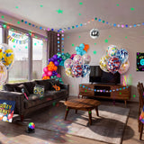 Complete kids glow disco birthday party decorations filling a living room, including confetti balloons, multicolour balloon garland, dot garland, glow star wall decorations, disco ball, disco ball, neon backdrop, table cover, microphone and boombox props from a OneStopBox all-in-one party kit.