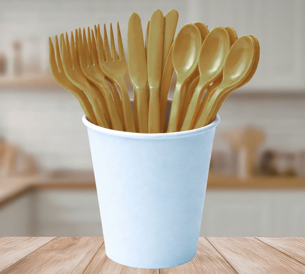 Set of gold reusable plastic cutlery in a white cup on a wooden table.