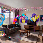 Complete K-Pop Demon Hunters themed kids birthday party decorations filling a living room, including character printed balloons, multicolour balloon garland, disco ball, triangle bunting, happy birthday banner, backdrop, disco ball, microphone props, glow sticks and themed table cover from a OneStopBox all-in-one party kit.