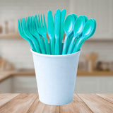 Light blue reusable plastic cutlery set in a white cup on a wooden table with a blurred kitchen background.