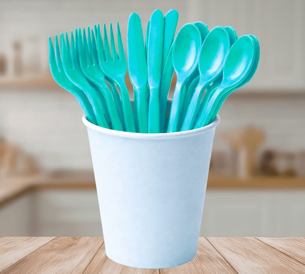 Light blue reusable plastic cutlery set in a white cup on a wooden table with a blurred kitchen background.