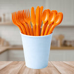 Orange reusable plastic cutlery set in a light blue cup on a wooden table.