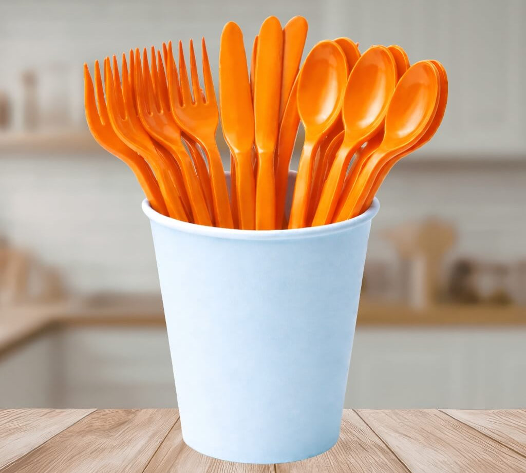 Orange reusable plastic cutlery set in a light blue cup on a wooden table.