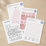 Set of birthday-themed activity sheets on a wooden surface for a pink themed birthday party