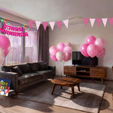 Living room decorated for a pink themed kids birthday party with pink and white balloons, pink triangle bunting, happy birthday banner, pink fringe curtain and pink table cover from a OneStopBox party decorations kit.