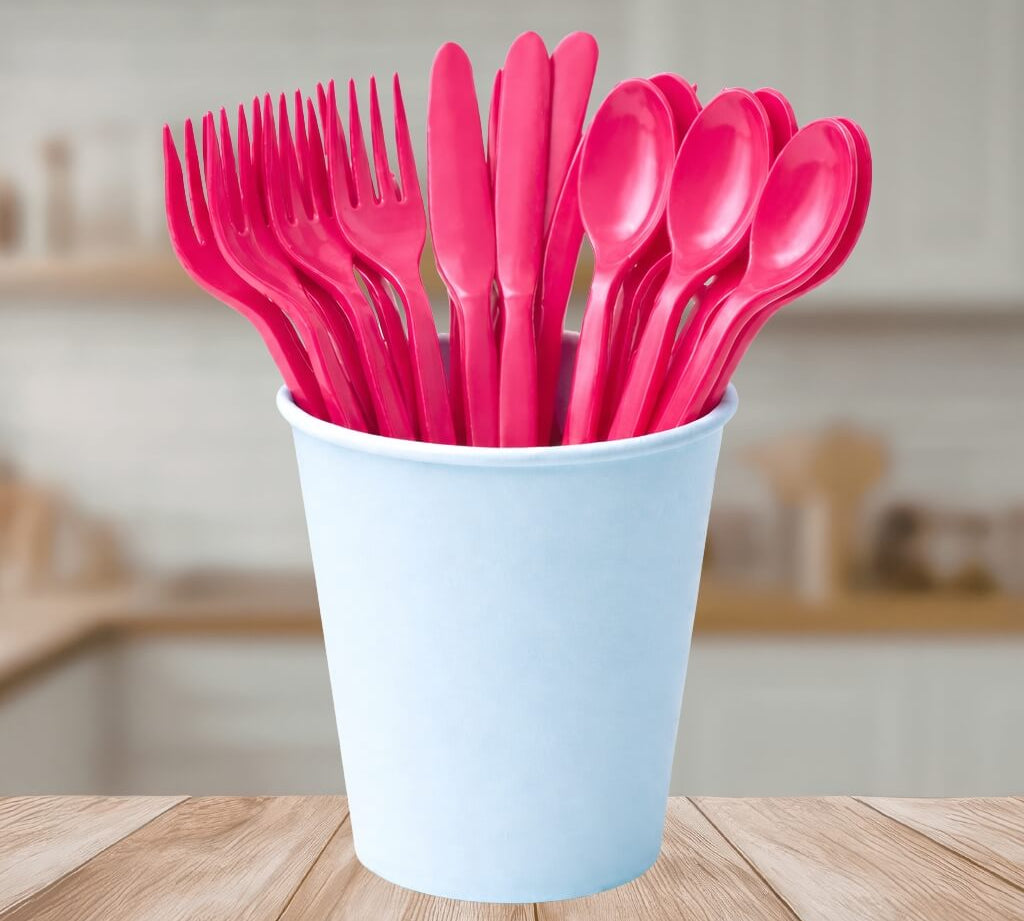 Set of pink reusable cutlery including forks, knives, and spoons in a light blue cup on a wooden surface.