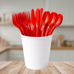 Red reusable plastic cutlery including forks, knives, and spoons in a white cup on a wooden table.