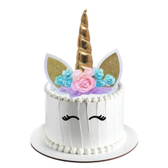 Unicorn-themed cake topper with gold horn, floral decorations, and white face with black eyes on a white background