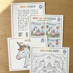 Educational activity sheets with unicorn theme on a wooden surface including word search, colouring and spot the difference